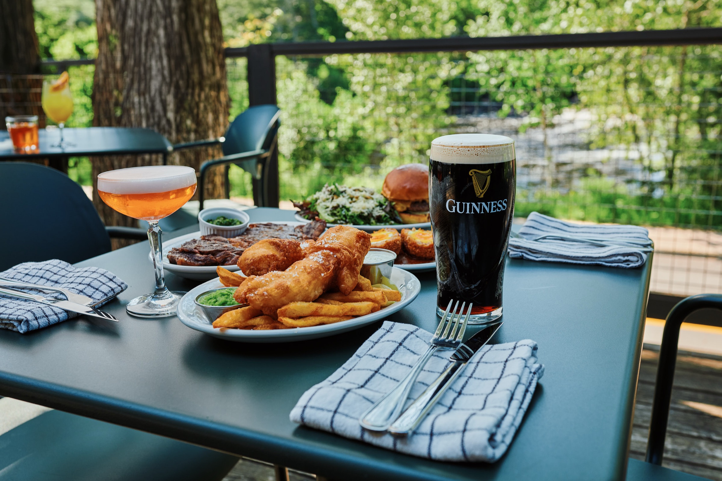 Fish and chips et pinte de Guinness sur la terrasse de MacTaverne, avec les arbres et la riviere de Val-David en arriere-plan.