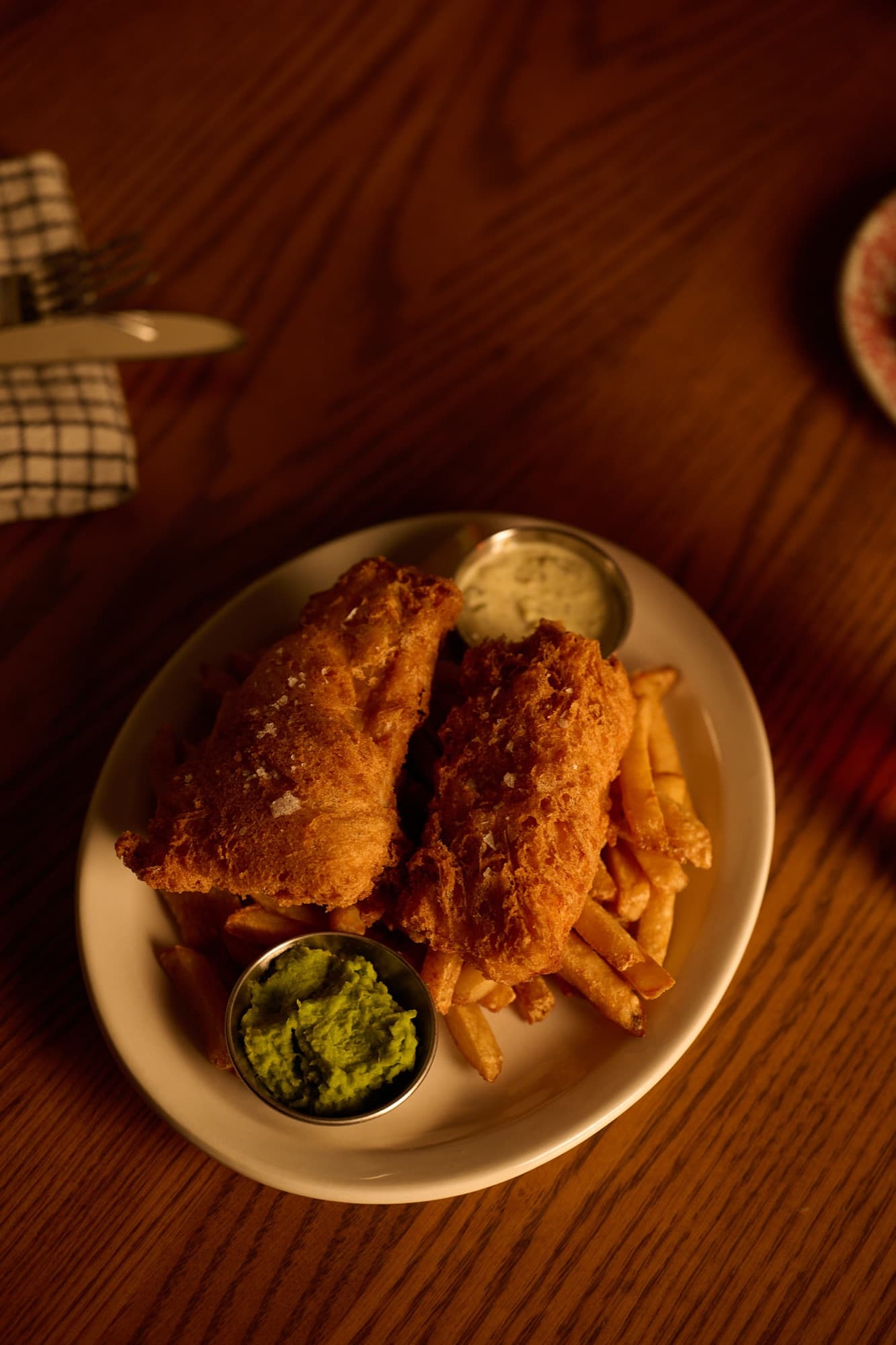 Golden beer-battered fish and chips with fries and mushy peas on a white plate, by candlelight